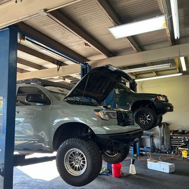 Two off-road vehicles lifted on car lifts in a garage, one with its hood open.