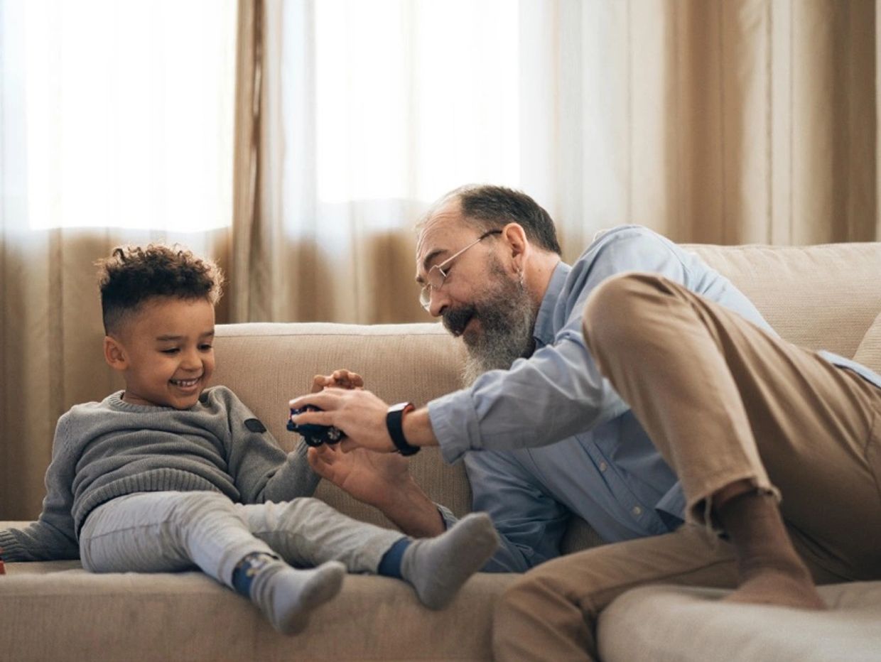 Grandfather playing with his grandson on the couch, sharing a joyful moment.