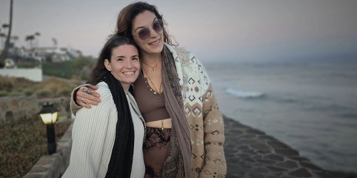 Two women warmly embracing by the seaside at dusk.