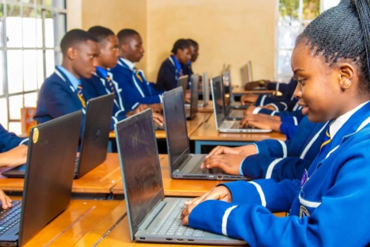 Students in blue uniforms working on laptops in a classroom.