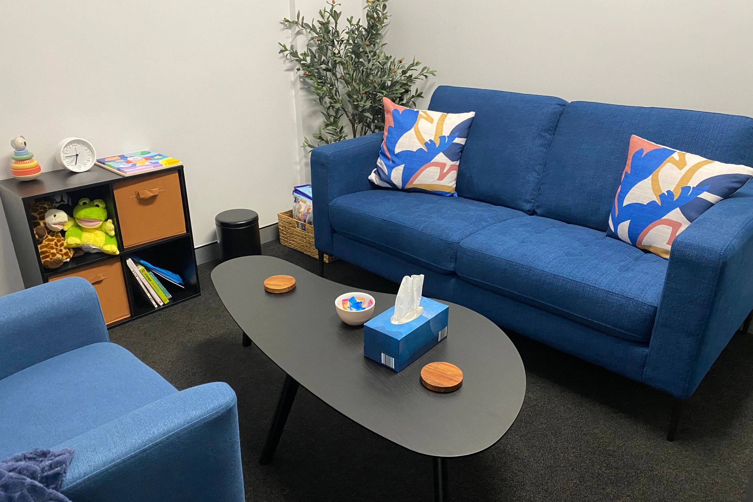 A welcoming, cosy office space with a blue couch, armchair, a black coffee table, and toys.