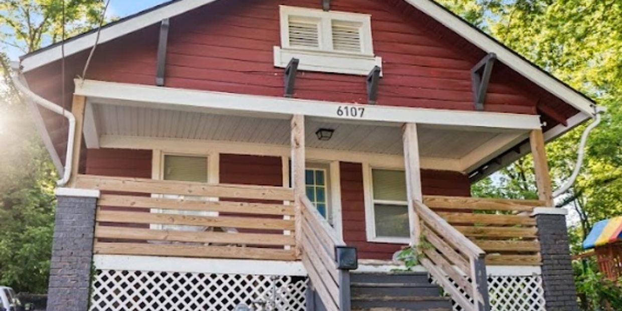 Red house with wooden porch and white lattice.