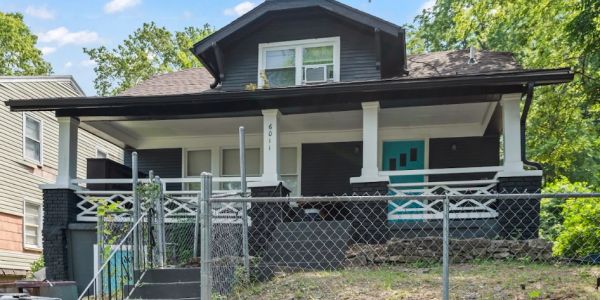 A dark-colored house with a turquoise door behind a chain-link fence.