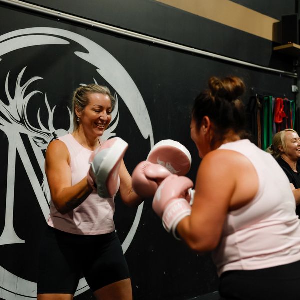 Women boxing in a gym, smiling and training together.