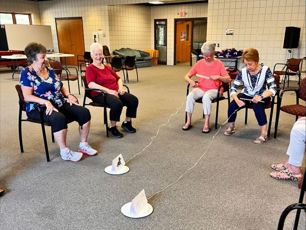Seniors in a seated group activity with string and paper cones.