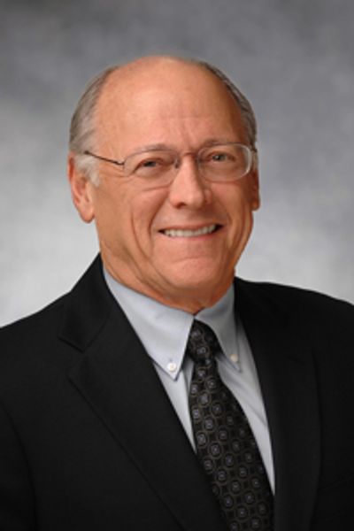Smiling elderly man in a suit and tie with glasses.