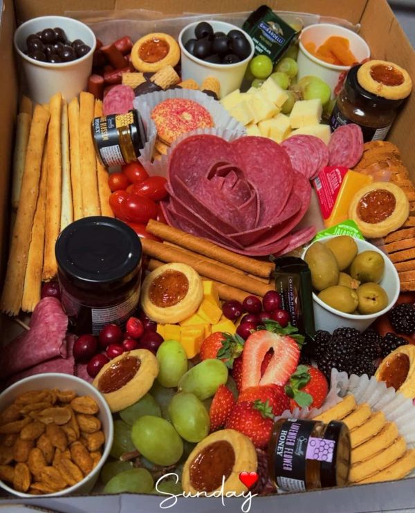 A vibrant charcuterie box with fruits, cheeses, meats, and snacks.