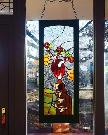 Stained glass panel with anatomical heart, flowers and mushrooms hanging in a window. "Limerence"