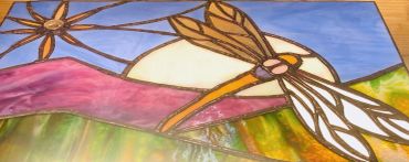 Stained glass artwork of a dragonfly and sun.