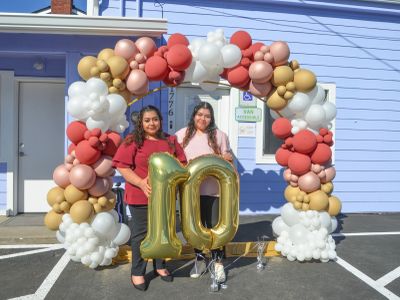 Two women posing under a balloon arch with gold number 10 balloons.