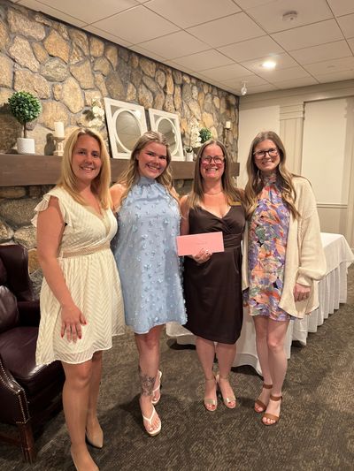 Four women dressed up, smiling in a cozy room with stone wall.