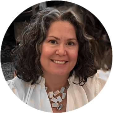 Woman in white shirt and a large silver necklace, with shoulder length greying hair, smiling