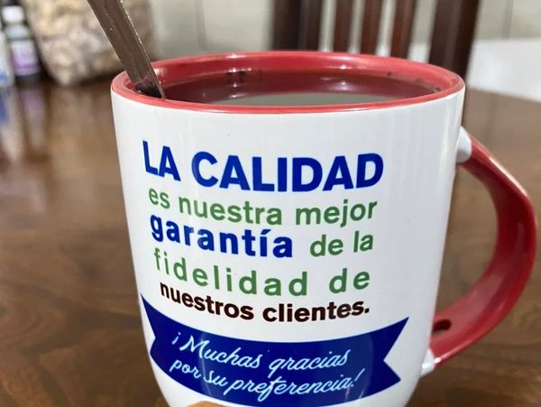 Taza con texto en español sobre calidad y fidelidad al cliente, con bebida y pan al frente.