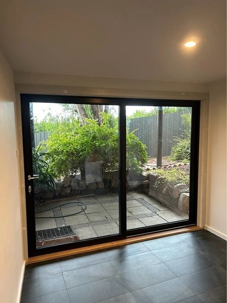 Sliding glass door opening to a small garden patio with greenery outside.
