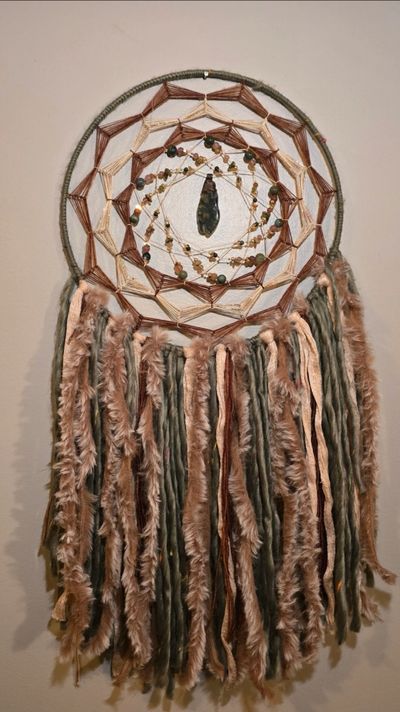 Handcrafted dreamcatcher with beads and soft fabric strands in earthy tones.