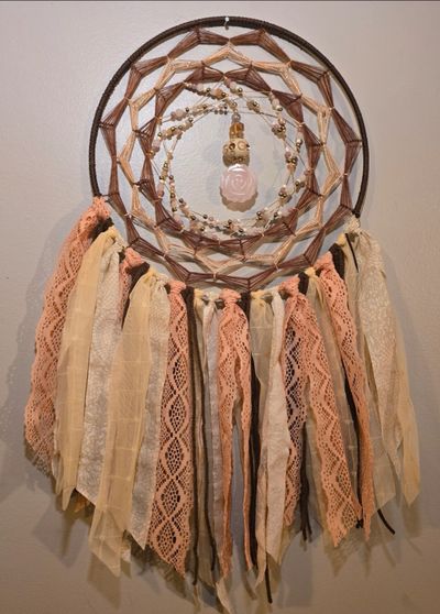 Decorative dreamcatcher with pink and beige ribbons and a hanging rose pendant.