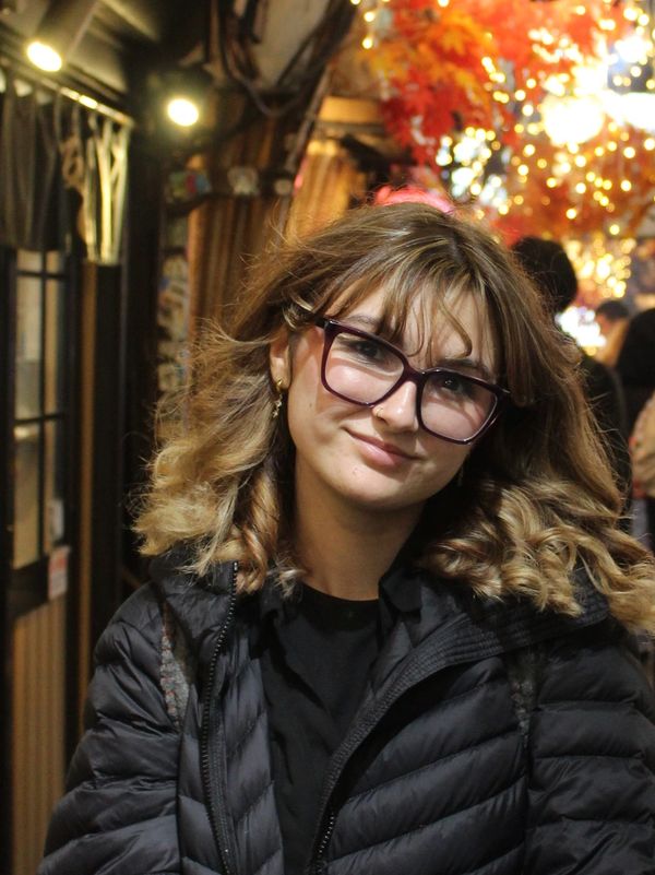 Young woman with glasses smiles warmly in a cozy, warmly lit setting.