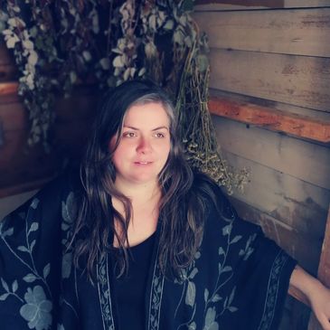 Woman with long hair wearing a dark floral shawl, sitting indoors.