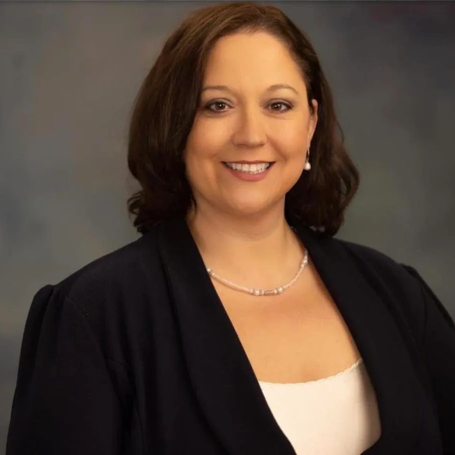 Smiling woman in professional attire with pearl necklace and earrings.