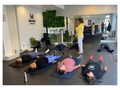 Cours de relaxation avec un instructeur debout et cinq participants allongés.