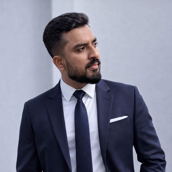 A confident man in a navy blue suit and tie looking sideways.