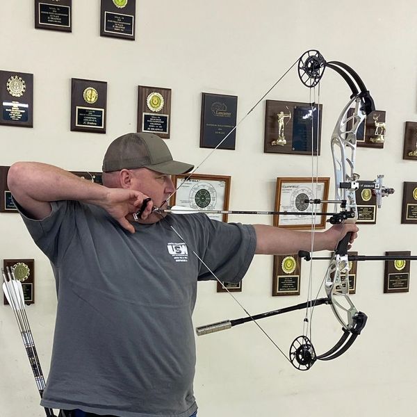 Man aiming with a modern compound bow indoors.