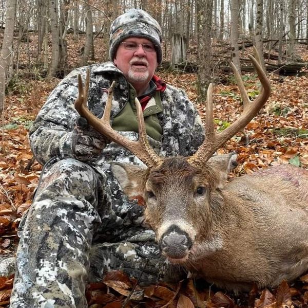 Hunter posing with a large buck deer in a forest.