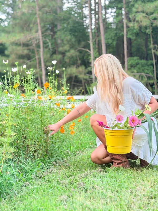 Woman picking flowers in a garden, holding a yellow bucket.