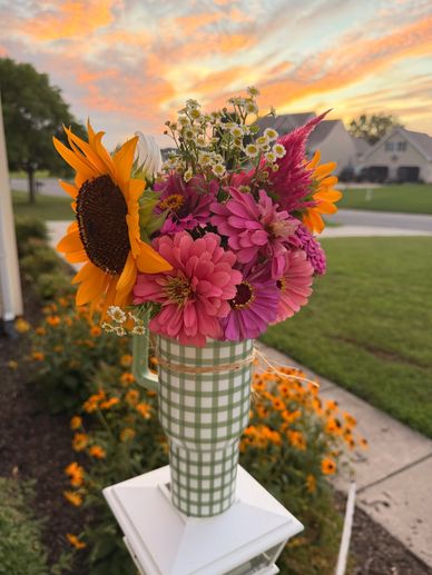 Vibrant bouquet of sunflowers and pink flowers in a plaid vase at sunset.