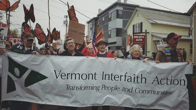 Clergy march carrying the VIA banner. Others have monarch butterfly cut-outs hoisted on poles.