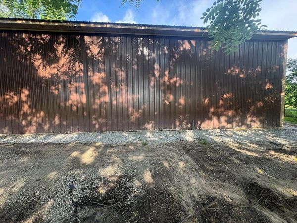 Brown metal wall with tree shadows on gravel ground.