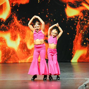 two tap dancers in pink costumes hip bumping on the ignite dance competition stage