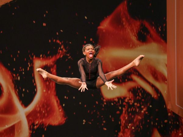 Young girl performing an energetic jump against a fiery background.