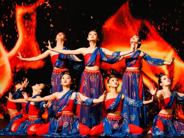 A group of dancers in traditional red and blue costumes looking up to the sky in a circle pose