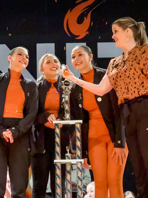 Group of three dancers in orange costumes winning a big overall trophy at Ignite Dance Competition
