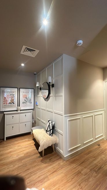 Cozy hallway with wooden flooring, white paneled walls, a small bench with a cushion, and framed Matisse prints.