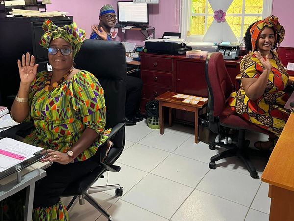 Three people in colorful traditional attire waving in an office.