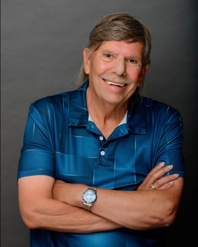 Smiling older man in blue shirt with arms crossed.