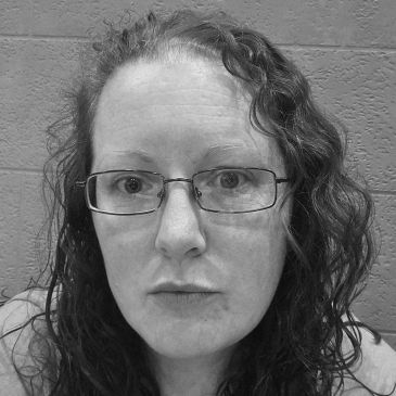 Black and white close-up of a woman with glasses and curly hair.