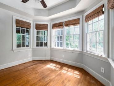 Empty corner room with wooden floors and multiple windows.