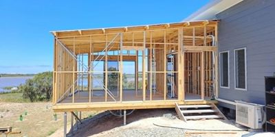 Wooden frame structure for a house extension near a lake.