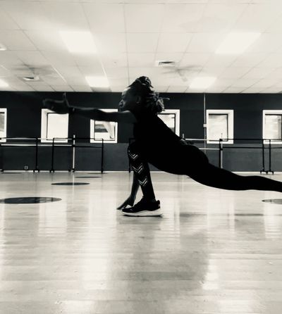 Person stretching in a spacious dance studio with large windows.
