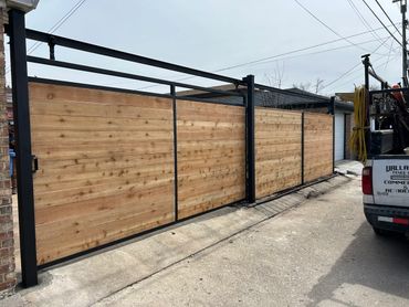 Modern wooden and metal sliding gate installed in a driveway.
