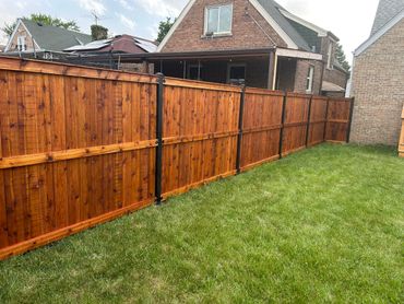 Freshly stained wooden fence with black metal supports around a suburban backyard.