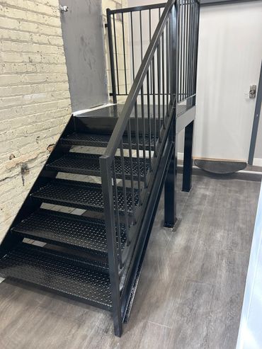Black metal staircase with railing in an industrial interior.