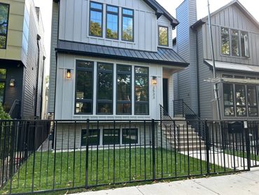 Modern two-story house with large windows and black metal fence.