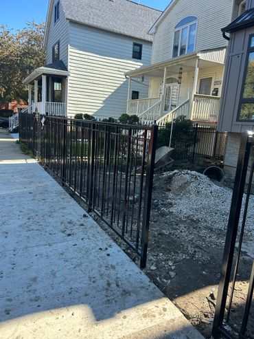 New black metal fence alongside a sidewalk near residential houses.