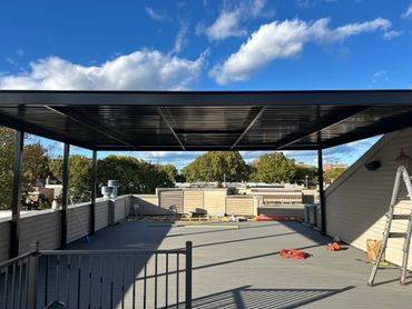 A rooftop patio with a modern black pergola under a blue sky.