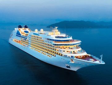 A large, illuminated cruise ship sailing on calm waters during twilight.