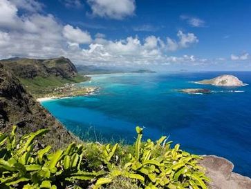 Scenic coastal view with lush greenery and clear blue ocean under a partly cloudy sky.